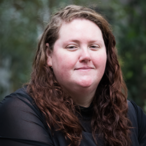 Photo of Anna smiling in front of a blurry outdoor background.